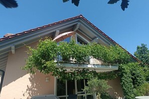 Een gebouw met een schuin dak, een balkon en een boom ervoor.