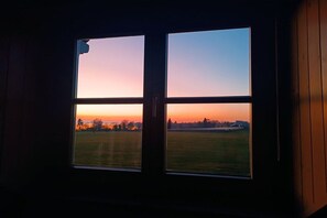 Een raam met uitzicht op een zonsondergang boven een grasveld.