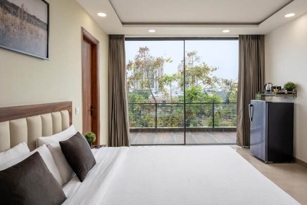 A hotel room with a large bed, a view of the city through a balcony, and a refrigerator.