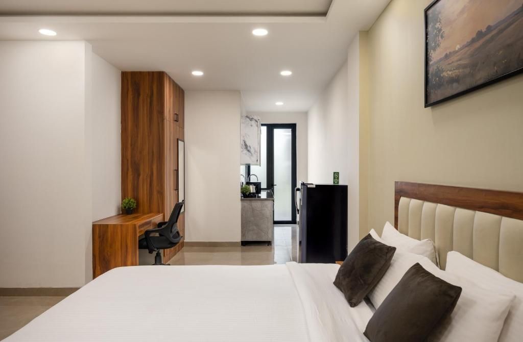 A modern hotel room with a large bed, a wooden desk, a small kitchenette, and a painting on the wall.