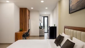 Et moderne hotelværelse med en stor seng, et træskrivebord, et lille tekøkken og et billede på væggen.