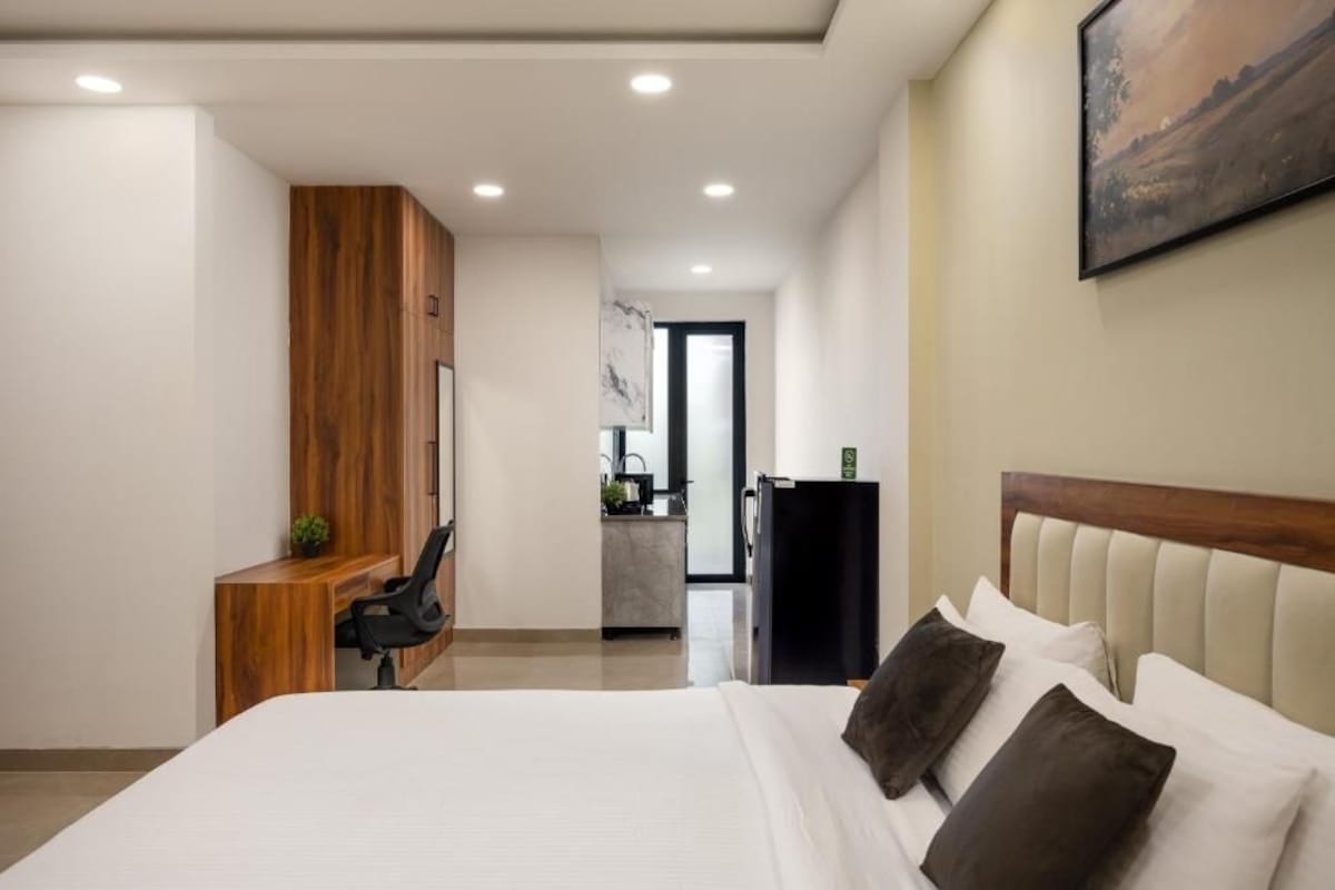 Quarto de hotel moderno com uma cama grande, uma escrivaninha de madeira, uma kitchenette pequena e um quadro na parede.