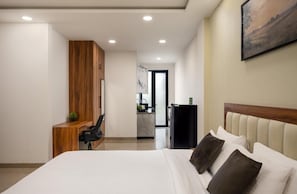 Quarto de hotel moderno com uma cama grande, uma escrivaninha de madeira, uma kitchenette pequena e um quadro na parede.