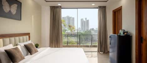 Habitación de hotel con una cama grande, ventilador de techo, vista de la ciudad por la ventana y refrigerador.