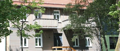 Un edificio de dos pisos con un balcón, una escalera de madera y una cerca.