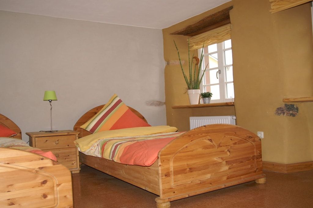 Une chambre à coucher avec un lit en bois, une table de chevet, une lampe et une fenêtre agrémentée d’une plante.