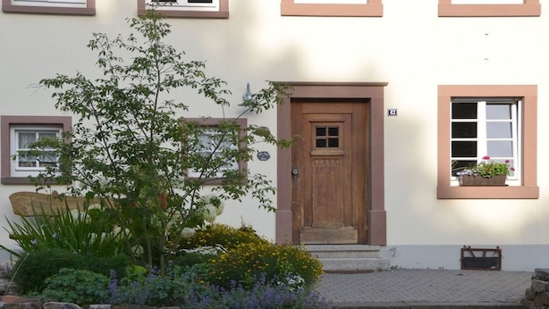 Un bâtiment doté d’une porte en bois, d’un mur en pierre et d’un petit jardin agrémenté de plantes et de fleurs.