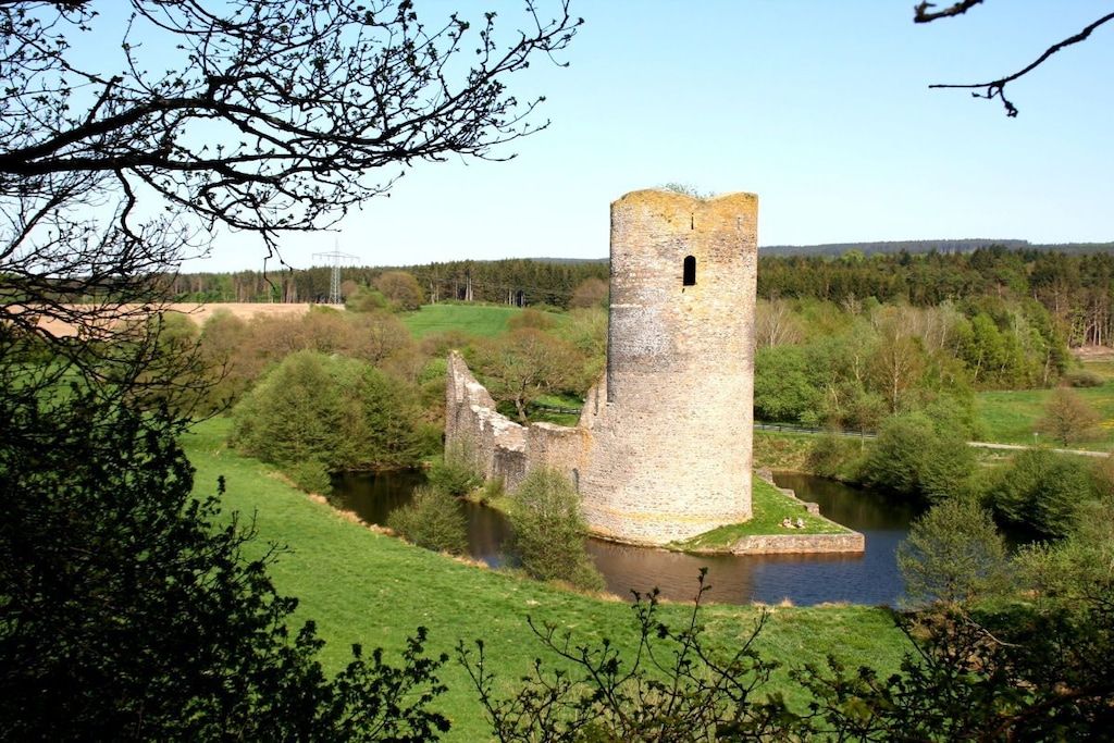 A historic stone tower surrounded by a moat and greenery.