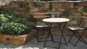 Un mur de pierre avec un banc en bois et une table ronde entourée de chaises.