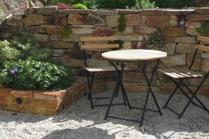 A stone wall with a wooden bench and a round table with chairs. - Holiday apartment with 1 bedroom (Morbach-Morscheid)