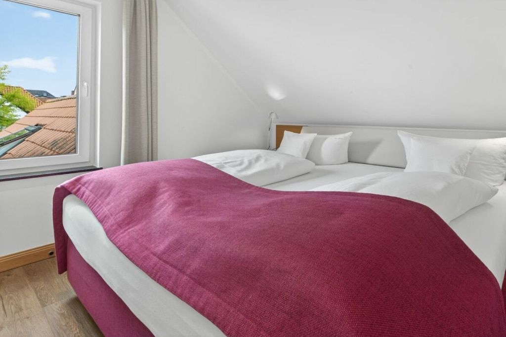 Un dormitorio con cama, ventana y vista a edificios.