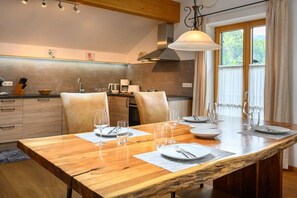 Een eetgedeelte met een houten tafel voor vier personen, een keuken op de achtergrond en een raam met gordijnen.