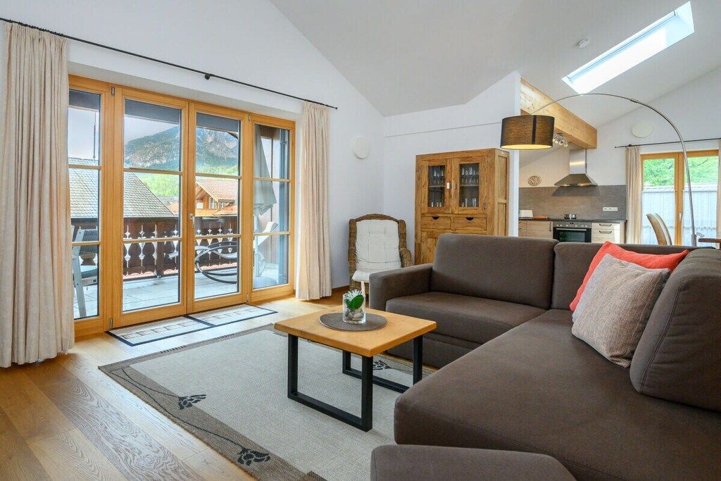 Un salon moderne avec un canapé, une table basse en bois et une vue sur un espace extérieur, accessible par de grandes portes vitrées.