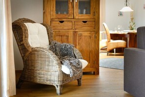 A wicker armchair with a white cushion and a leopard print throw blanket, positioned in a room with wooden cabinets and a dining area in the background. - Holiday apartment with 2 bedrooms (Farchant)