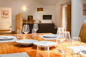 Taula de dinar preparada per a quatre amb gots de vi i plats, un armari de fusta, una televisió i un sofà al fons.