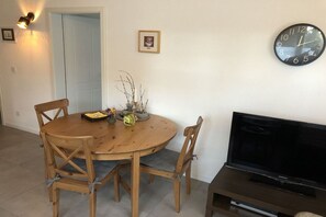 A dining area with a round wooden table, four chairs, a wall clock, a flat-screen TV, and a door in the background. - Holiday apartment with 1 bedroom (Segnitz)