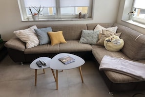 A living room with a sofa, two side tables, and a window with blinds. - Holiday apartment with 1 bedroom (Segnitz)