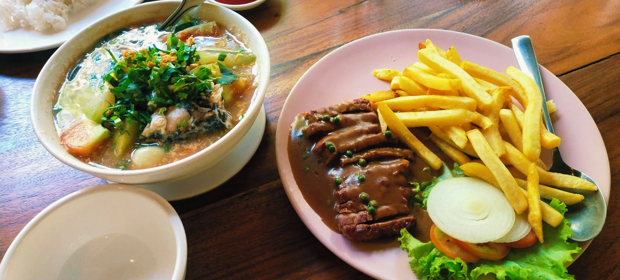 Una comida que incluye una sopa de verduras y carne, un plato de carne en rodajas con papas fritas y un tazón de arroz.