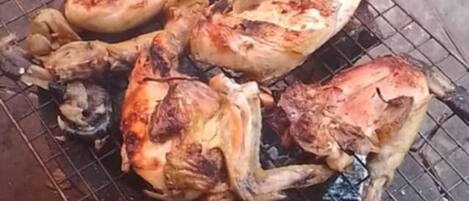 A grill with several pieces of meat cooking on a hexagonal stone pavement.