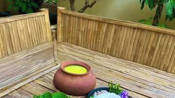 A traditional meal setup with various dishes and utensils on a wooden table, surrounded by greenery.