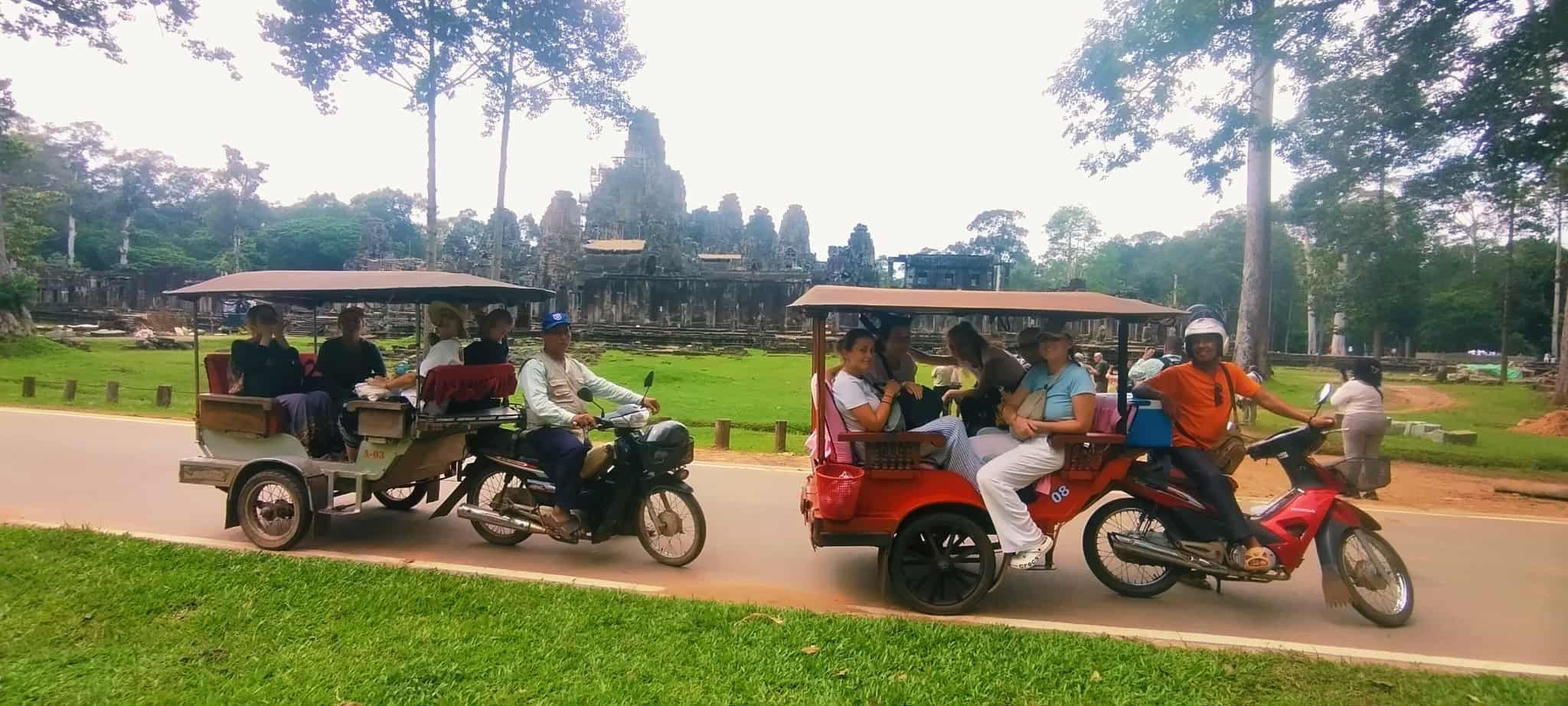 Un groupe de personnes est assis sur une moto rouge avec un side-car, et ils roulent sur une route bordée de verdure, avec des arbres en arrière-plan.