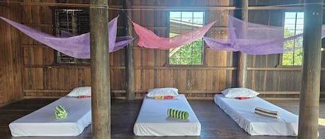A room with three single beds, wooden walls, and a large window.