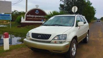 Um SUV branco estacionado em uma estrada rural, com uma placa indicando 'Sambor Preuk Tempel Sute' ao fundo.