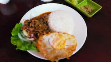 A plate with rice, a fried item, and a meat dish, accompanied by a green condiment dish.