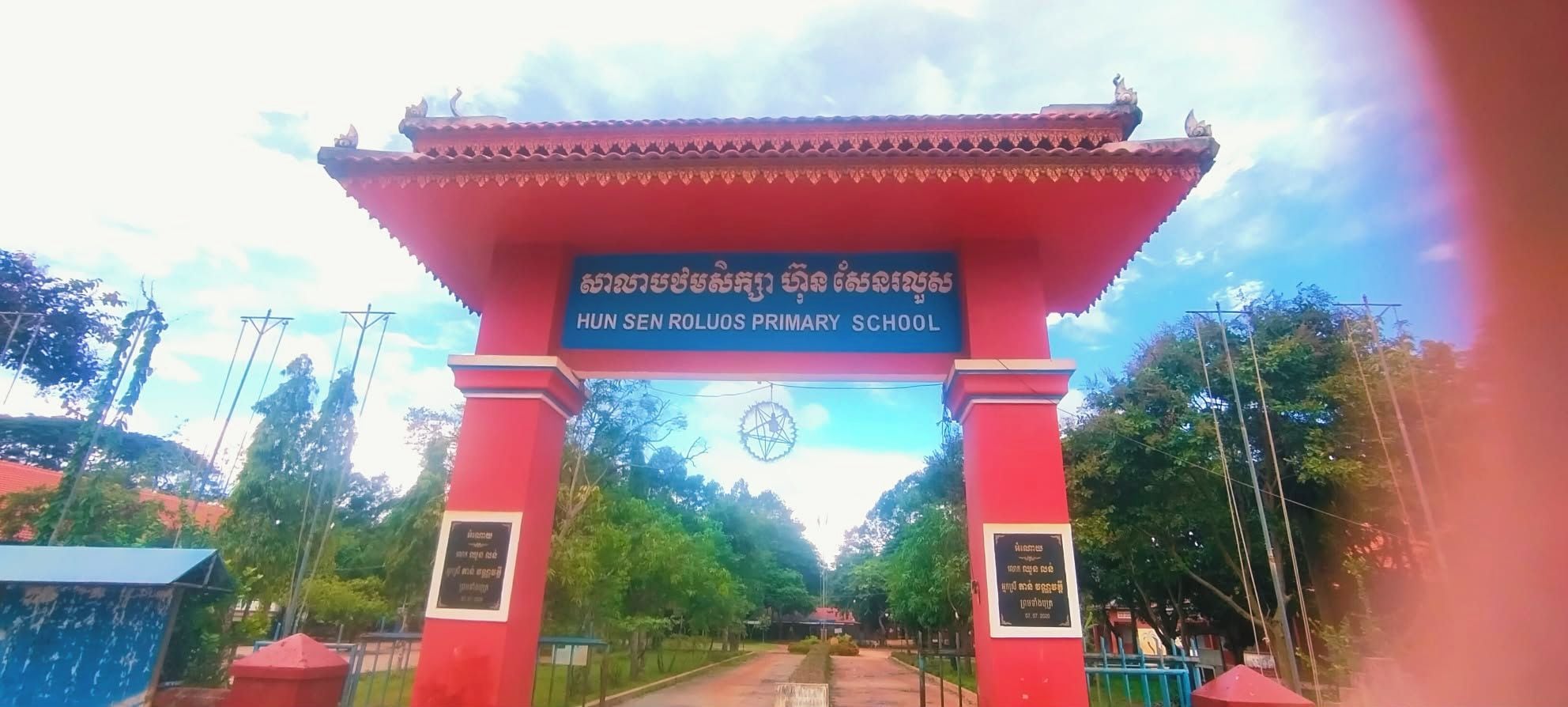 Un arco rojo con un letrero que indica la Escuela Primaria Hun Sen Roluos.