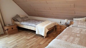 Una camera da letto con soffitto spiovente, un letto con copripiumino decorato, un comodino con una lampada e un tavolino notte con un piccolo oggetto sopra.