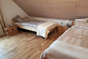 Un dormitorio con techo inclinado, una cama con colcha estampada, una mesita de noche con lámpara y un mueble auxiliar con un objeto pequeño encima.