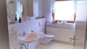 Un bagno con lavandino, wc, specchio e finestra con tende.