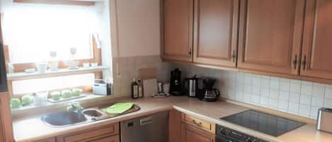 Cocina con gabinetes de madera, lavavajillas, horno y ventana con vista al exterior.
