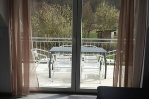 A balcony with metal chairs and a table, a sliding glass door, and a view of trees and a building in the background. - Holiday apartment with 3 bedrooms (Werbachhausen)