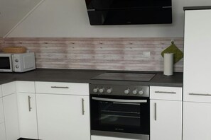 Eine Küche mit weißen Schränken, einer Mikrowelle, einem Herd und einem an der Wand befestigten Flachbildfernseher.
