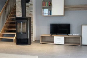 A modern living room with a fireplace, a television, a bookshelf, and a staircase. - Holiday apartment with 3 bedrooms (Werbachhausen)