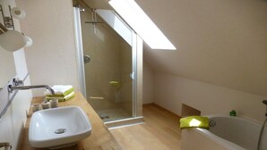 A modern bathroom with a wooden vanity, a white sink, a glass shower enclosure, and a bathtub. - Holiday home in Oberharmersbach with sauna (Oberharmersbach)