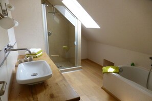 Een moderne badkamer met een houten wastafelmeubel, een witte wasbak, een douchecabine van glas en een bad.