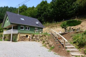 Una casa amb teulada inclinada, parabrella satèl·lit, un porxo i una escala que condueix a un parasol verd.