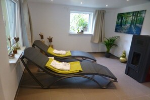 A room with two reclining chairs, a window with curtains, a painting, a plant, and a television. - Holiday home in Oberharmersbach with sauna (Oberharmersbach)