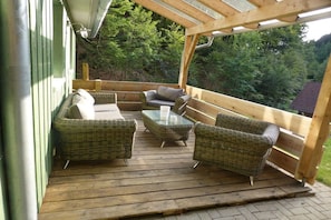 A covered outdoor deck with wicker furniture and a glass table. - Holiday home in Oberharmersbach with sauna (Oberharmersbach)