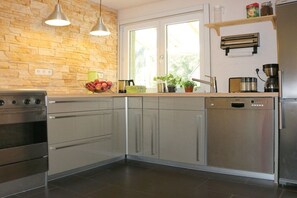A modern kitchen with stainless steel appliances, a stone backsplash, and a window providing natural light. - Holiday home in Oberharmersbach with sauna (Oberharmersbach)