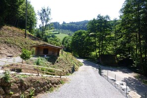 Un camí de grava que condueix a una petita cabana de fusta envoltada d'arbres i turons.
