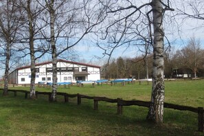 A building with a white facade and dark trim, surrounded by a grassy area with birch trees. - Holiday apartment with 1 bedroom (Neuried)