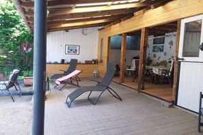 Ein überdachter Patio-Bereich mit Liegestühlen, einem Tisch und einer Holzbalkendecke.
