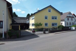A yellow two-story residential building with a gated entrance, a satellite dish, and a small garden area. - Holiday apartment with 1 bedroom (Neuried)