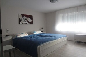 Un dormitorio con cama, mesitas de noche, radiador y ventana con persianas.