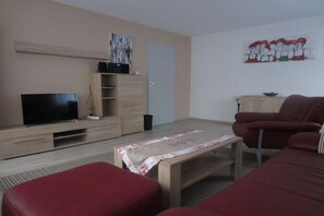 A living room with a television, a wooden cabinet, a red sofa, and a painting on the wall. - Holiday apartment with 1 bedroom (Neuried)