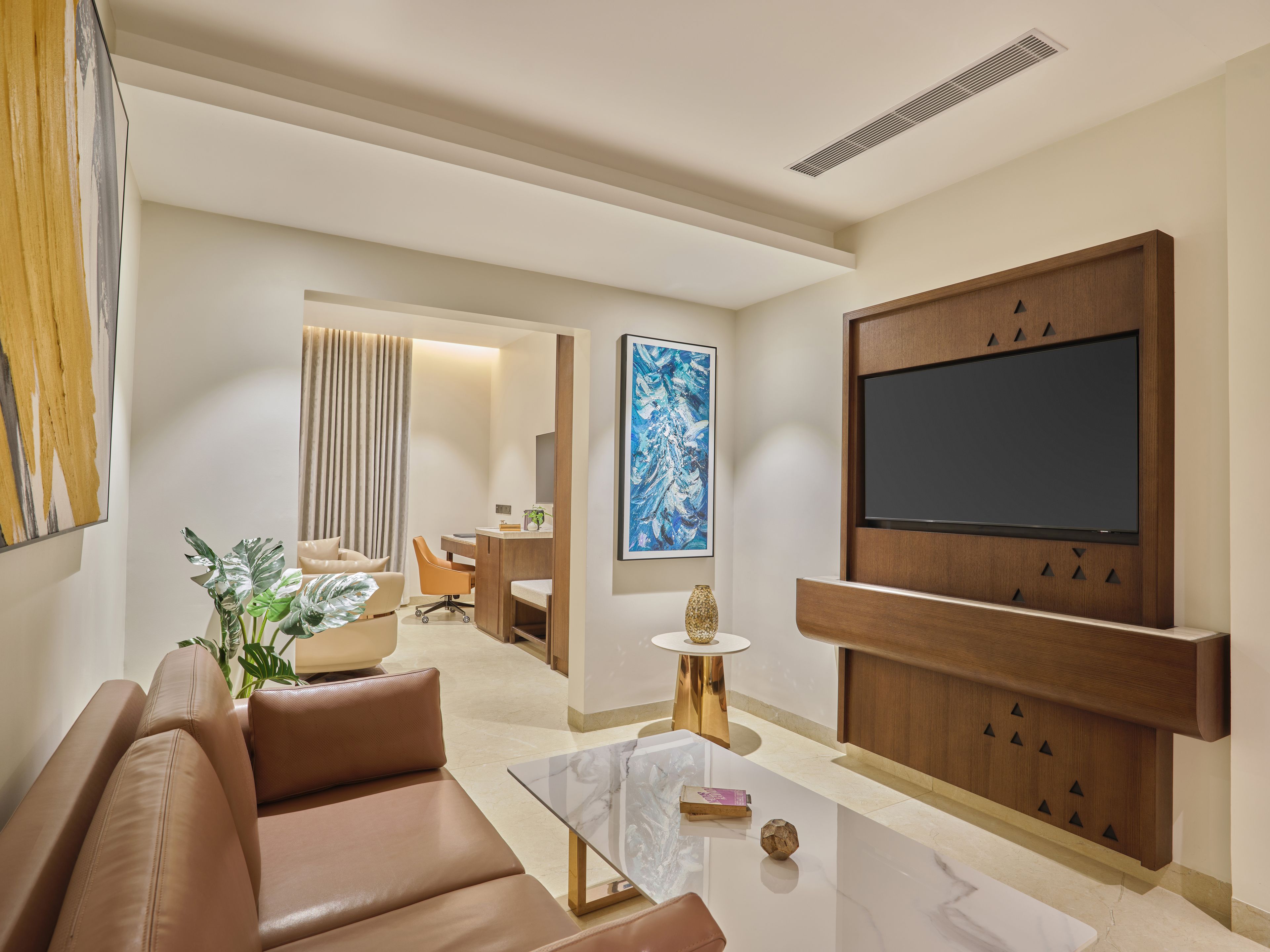 A modern living room with a leather sofa, a coffee table, a TV mounted on a wooden panel, and a plant.