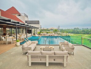 A rooftop pool area with lounge seating and a view of a golf course. - Crowne Regency (Meenachil)